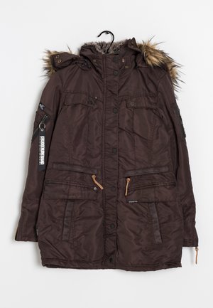 Veste d'hiver marron foncé avec capuche bordée de fourrure, boutons-pression à l'avant, plusieurs poches, poche zippée sur la manche et étiquette de marque sur le bras gauche.