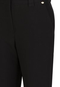 Schwarze Hosen aus einem Stoff mit glatter Textur, mit seitlichen Taschen und einem kleinen Metallakzent nahe dem Bund.