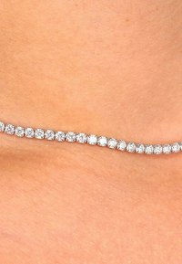 Rhinestone chokerhalskæde med en kontinuerlig række af cirkulære klare sten indsat i sølvfarvet metal, glat overflade og fleksibelt design.