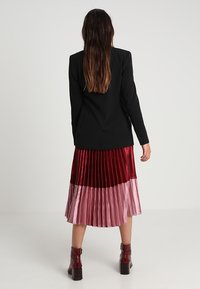 Black blazer with a fitted design paired with a pleated, color-blocked skirt in burgundy, rose, and pink velvet. Includes ankle boots.