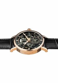 Skeletonur med ett hus i roséguld i rostfritt stål, svart urtavla som visar de inre mekanismerna, och ett svart läderarmband.