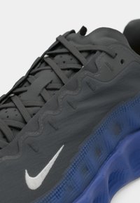 Μαύρο αθλητικό παπούτσι με κυματιστό σχέδιο, υφασμάτινη επιφάνεια, γκρι κορδόνια και μπλε διαφανή σόλα. Διαθέτει το λευκό λογότυπο της Nike.