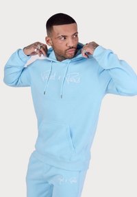 Felpa leggera blu con cappuccio e coulisse, dotata di tasca frontale, con testo bianco "Project x Paris." Materiale morbido in misto cotone, vestibilità rilassata.
