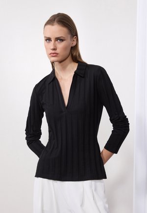 Black long-sleeve shirt with a V-neck and collar, featuring vertical ribbed texture and fitted design. Worn with white pants.