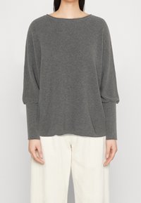 Maglione grigio a coste con maniche lunghe e scollatura ampia, abbinato a pantaloni larghi di colore chiaro. Tessuto morbido, design rilassato.