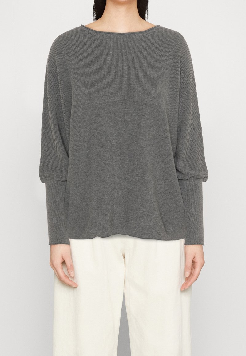 Maglione grigio a coste con maniche lunghe e scollatura ampia, abbinato a pantaloni larghi di colore chiaro. Tessuto morbido, design rilassato.