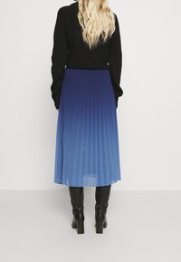 Blå plisserad midikjol med en ombre-effekt som övergår från mörk till ljusblå, kombinerad med svarta klackstövlar och en svart stickad topp.