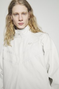Hvid Nike quarter-zip pullover med høj krave, prydet med blødt stof, frontpanel med chevron-detaljer og diskret logo-broderi.