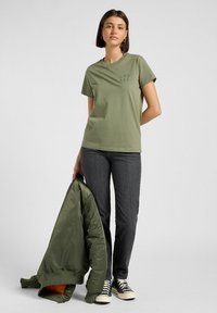 Oliwkowa bawełniana koszulka z krótkim rękawem i okrągłym dekoltem. Połączona z ciemnoszarymi dżinsami i zieloną kurtką bomber.