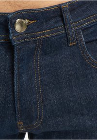 Mørkeblå denimjeans med kontrasterende oransje sømmer, metallknapp, og et klassisk design med fem lommer.