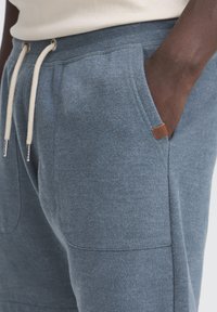 Shorts joggers en coton bleu avec taille élastique, fermeture à cordon de serrage, poches latérales et une petite étiquette en cuir marron de la marque.