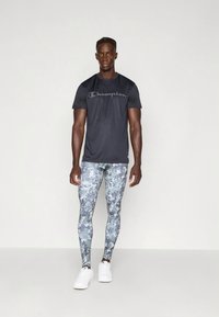 Zwart sportt-shirt met "Champion"-logo, gecombineerd met nauwsluitende camouflageleggings in tinten grijs en blauw. Witte sportschoenen maken de outfit compleet.