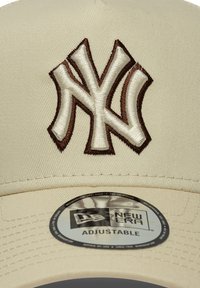 Ρυθμιζόμενο μπεζ καπέλο με ανάγλυφο καφέ κεντημένο λογότυπο New York Yankees. Διαθέτει κυκλικό αυτοκόλλητο αυθεντικότητας New Era στην γείσα.