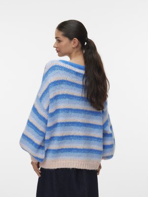 Kvinde med langt mørkt hår samlet i en hestehale, iført en blå, hvid og lyserød stribet striktrøje, set fra siden mod en ensfarvet baggrund.