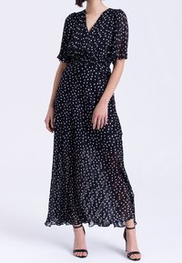 Czarna maxi sukienka w białe kropki z krótkimi bufkami i dekoltem w kształcie litery V; posiada elastyczny pas i zwiewny materiał dla lekkiego uczucia.
