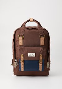 Brun nylon ryggsekk med en marineblå frontlomme, tan lærdetaljer, messingbeslag og justerbare stropper. Har en merkevarelabel.