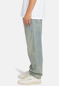Lichtblauwe dennen jeans met een rechte pijp, voorzien van een vervaagde wasbeurt, vijf zakken en een versleten uitstraling, gecombineerd met witte sneakers.