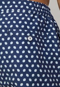Dunkelblaue Badehosen mit einem weißen Muschel-Muster, elastischem Bund und einer Gesäßtasche mit einem Knopfdetail.