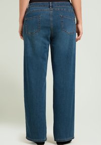 Vaqueros de mezclilla azul de pierna ancha con cinco bolsillos, costuras sutiles y una textura suave. La cintura presenta un diseño estándar.