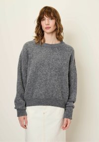 Siva pletena oversize pulover s dolgimi rokavi, rebrastimi manšetami in robom. Mehak, teksturiran material. Uporabljen z belo krilom.