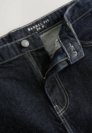 Dark blue denim jeans with a zip fly, silver button, and white stitching. Label reads "BARREL FIT 34 R." Front pocket opening is visible.