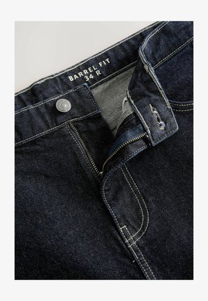 Donkerblauwe denim jeans met een ritssluiting, zilveren knoop en witte stiksels. Het label vermeldt "BARREL FIT 34 R." De opening van de zijzak is zichtbaar.