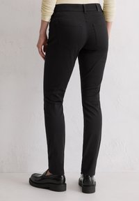 Zwarte slim-fit broek met een gladde textuur en een klassiek ontwerp. Beschikt over een tailleband, achterzakken, en wordt gedragen met zwarte instappers.