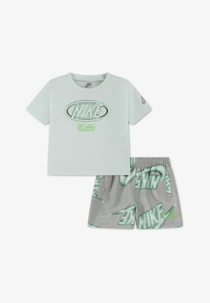 T-shirt Nike vert clair à manches courtes avec un grand logo et un short vert-gris recouvert de logos Nike surdimensionnés.