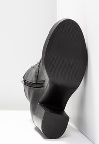 Botte en cuir noir avec une semelle texturée, un talon carré et un détail de fermeture à glissière sur le côté. Tige lisse avec des accents matériels minimalistes.