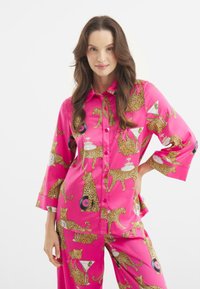 Růžový saténový pyžamový set s leopardími vzory, gramofonovými deskami a sklenkami na martini. Košile má límcový design a široké rukávy.
