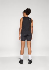 Top atletico senza maniche nero con logo, abbinato a pantaloni corti neri aderenti. Modello con calzini bianchi e scarpe nere. Tessuto liscio e leggero.