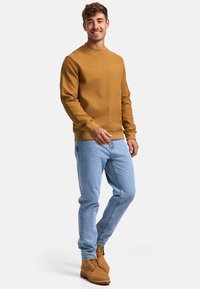 Sudadera de punto acanalado mostaza, jeans de mezclilla azul claro y botas tan con cordones. Presenta un cuello redondo y puños ajustados. Diseño simple y texturizado.