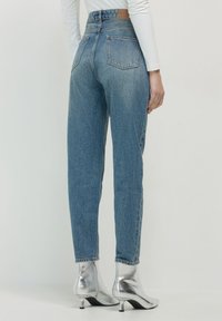 Jean en denim léger bleu clair taille haute avec une coupe décontractée, dotés de poches arrière et d'une étiquette en cuir marron à la taille.