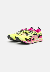 Baskets de sport jaunes fluo avec accents noirs, doublure rose et semelle multicolore. Présente un dessus en mesh texturé et des détails à motifs.