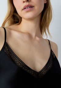 Zwarte satijnen top met een kantafwerking langs de V-halssnit en dunne, verstelbare bandjes. Gladde textuur met gedetailleerde kantaccenten.