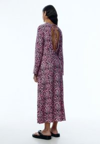 Langärmliges rosa Kleid mit Leopardenmuster, offener Rückseite und Bindedetail, aus weichem Stoff gefertigt, kombiniert mit schwarzen flachen Sandalen.