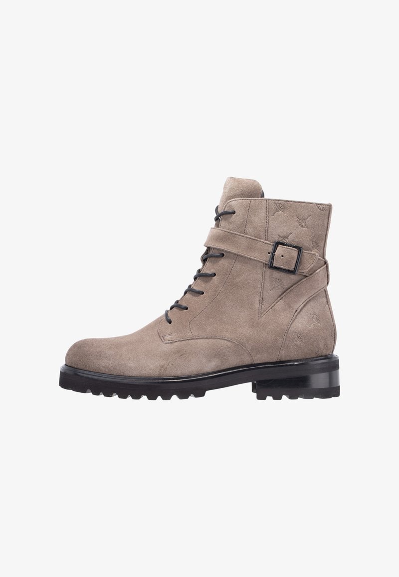 Stivaletti alla caviglia in camoscio color taupe chiaro con chiusura frontale con lacci, dettaglio con fibbia e texture, poggiati su una suola nera robusta.