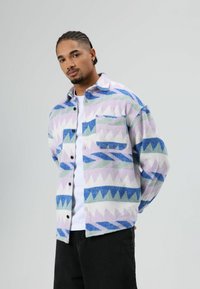 Kleurrijk fleece shirt met een geometrisch patroon in pasteltinten paars, blauw en groen. Voorzien van een borstzak en knoopsluiting.