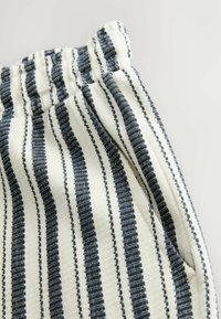 Tissu rayé avec des teintes bleu marine et blanc cassé, avec une surface texturée. Ceinture élastique visible en haut, mettant en avant des motifs verticaux.