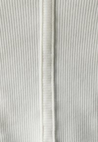 Tissu blanc à texture côtelée verticale, avec une couture centrale qui descend au milieu. Matière douce et légèrement extensible.