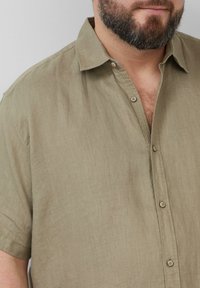 Kurzärmliges, olivgrünes Leinenhemd mit Button-Down-Kragen, Holzkneifen und einem leicht strukturierten, atmungsaktiven Stoff.