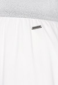 Witte jurk met een gestructureerde zilveren top, soepelvallende rok en een klein metalen logo-label "DREIMASTER" dicht bij de zoom.