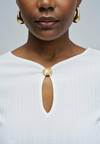 Top blanco texturizado con escote en forma de lágrima y un acento decorativo de hardware dorado en el centro. Diseño elegante y minimalista.