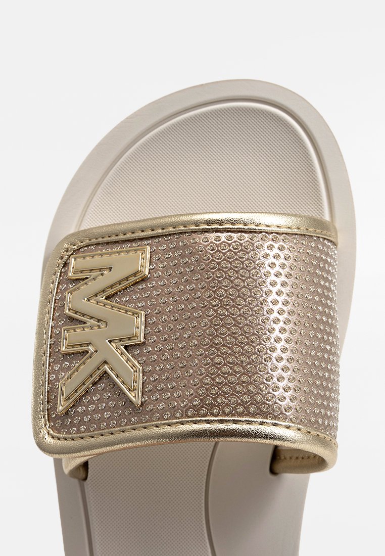 Sandale à glissière avec une sangle métallique dorée texturée, présentant des détails perforés et un logo bien visible. Semelle beige douce.