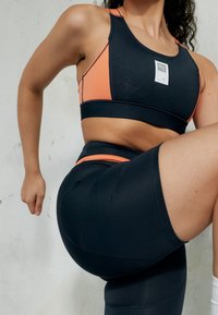 Svart sport-bh och högmidjade shorts med orange accenter. Slät, elastisk tyg och en logotypapplikation på bh:n.