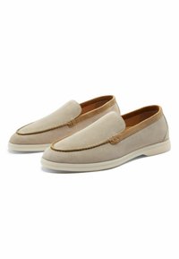 Scarpe slip-on in suede beige con punta arrotondata, bordi in pelle marrone a contrasto e suole in gomma leggera. Dettagli di cucitura lungo le cuciture.