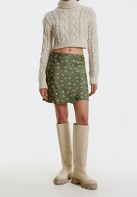 Kerman pienohahtipulloveri, vihreä kukkakuosiseksi mini-hame ja beige polven ylle ulottuvat saappaat, joiden pohjat ovat paksut. Tekstuuriset materiaalit näkyvät.