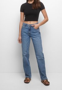 Jean en denim bleu clair à coupe droite, taille haute, design à cinq poches et fermeture par bouton. Associé à un t-shirt noir court.