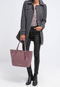 Grijze wollen jas, bloemen top, zwarte skinny jeans en zwarte enkellaarsjes. Paarse textuur schoudertas met lange banden en een metalen accent.
