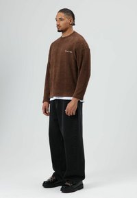 Bruine fleece trui met een textuurrijke afwerking, gecombineerd met wijde zwarte denim broek en zwarte schoenen met roze veters.